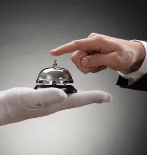 A person in a suit presses a service desk bell resting on the gloved hand of another person.