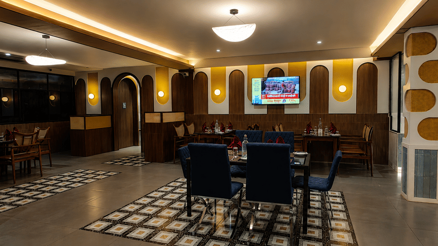 Contemporary dining space with centrally arranged tables, upholstered chairs, ambient ceiling lighting, and a wall-mounted television at Kali Mirch Restaurant, Lords Riverside Resort, Muduba.