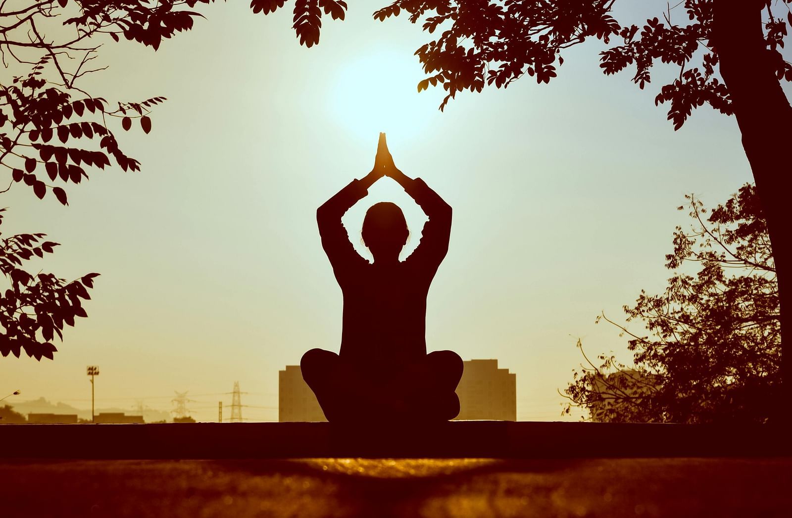 A person in a yoga pose with their hands above their head, silhouetted against a bright background. 