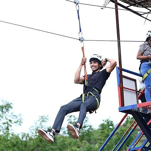 An overview of a person performing a zip lining activity with people on top looking - Diamond Parks, Pune.