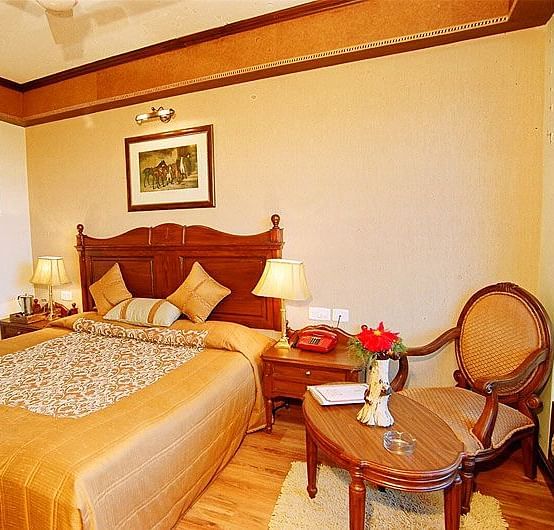 View of a bedroom with a small table and chair and a bed with side drawers on each side - Sun N Snow Inn, Kausani