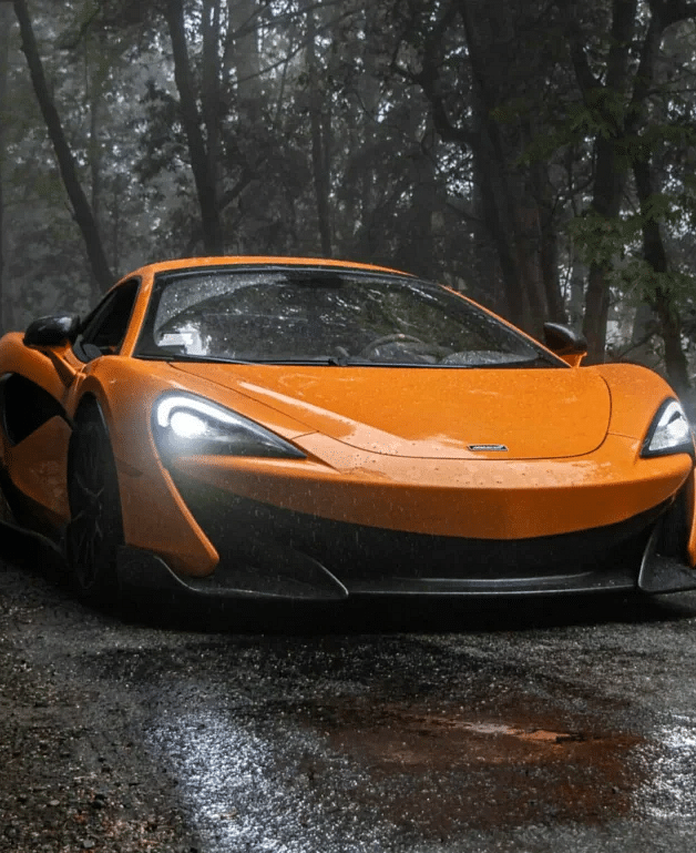 an orange colored sports car driving through a wet muddy trail