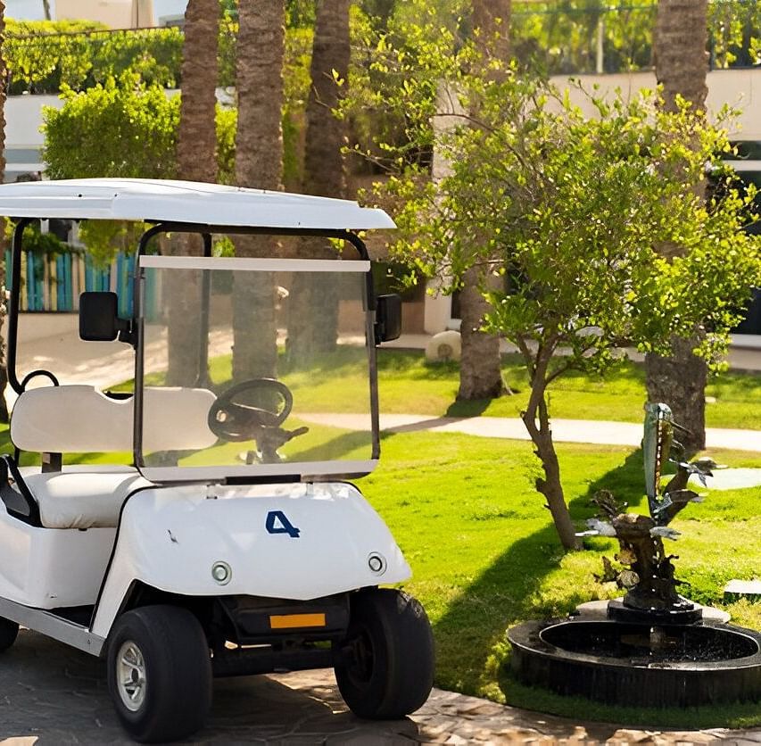 A white golf cart parked near a building surrounded by greenery.