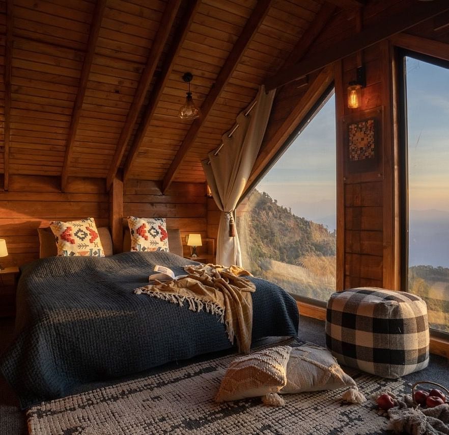 An image of a attic room with king size bed with a huge window providing a view of mountains - Avalon Cottages, Kanatal