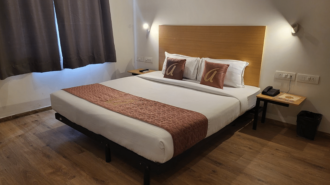 A comfortable hotel room with a double bed, brown accents, warm lighting, and dark curtains for privacy - Astra Hotels & Suites, Sarjapura