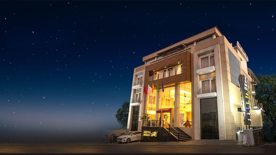 A multi-storey building with illuminated windows and a prominent entrance stands under a dark, star-filled night sky - Mansha Regency, Port Blair