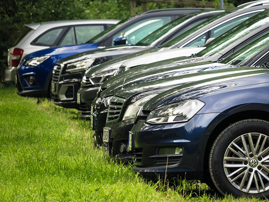 A number of cars parked in a lawn with green grass