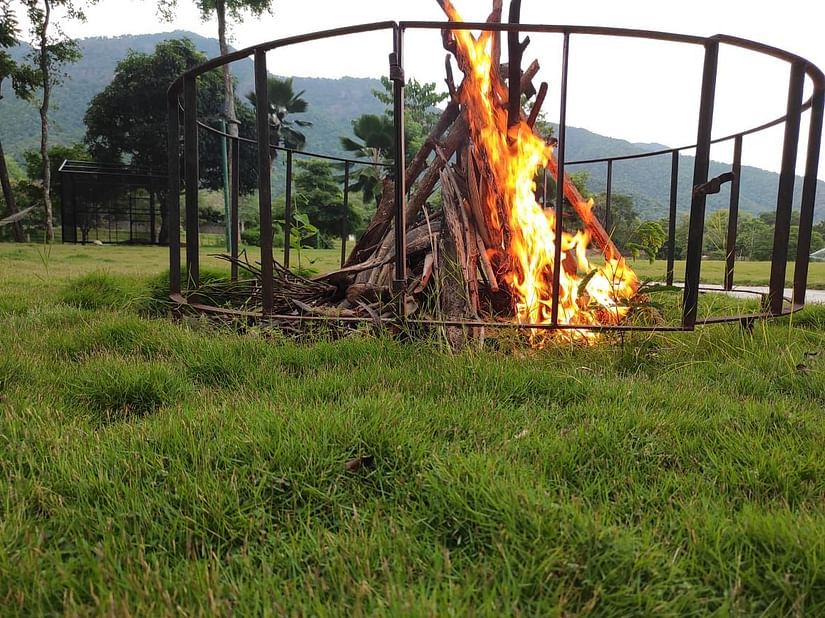 A large bonfire set up in a grassy area surrounded by protective fencing, ready for an evening gathering - Black Thunder, Coimbatore