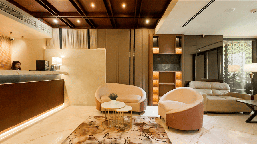 A wide-angle shot of the lobby at F Hotels, Bengaluru, featuring the common seating area with a coffee table placed atop a modern-style rug, along with the reception desk in the corner.