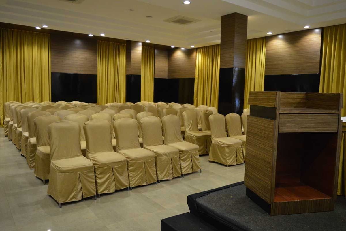 A large banquet hall at The Royal Comfort, set up for a conference or event with rows of chairs facing a stage with a podium, all under warm lighting.