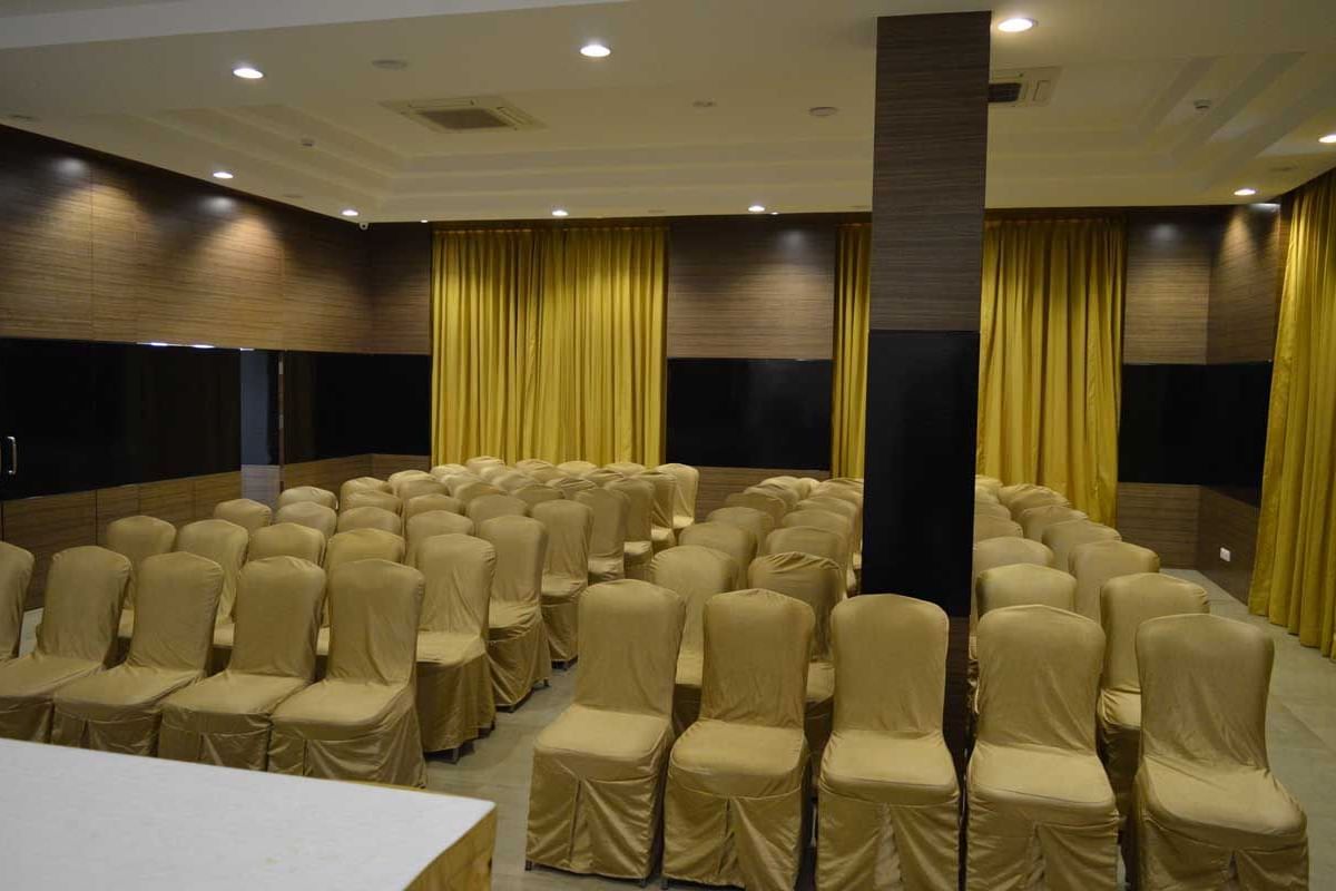 A large banquet hall at The Royal Comfort, set up for a conference or event with rows of chairs facing a stage with a podium, all under warm lighting.