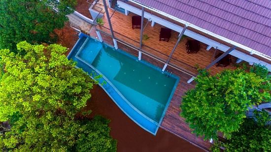  A swimming pool with an edge blending into the forested background, reflecting the trees and sky.- Abad Brookside Lakkidi, Wayanad