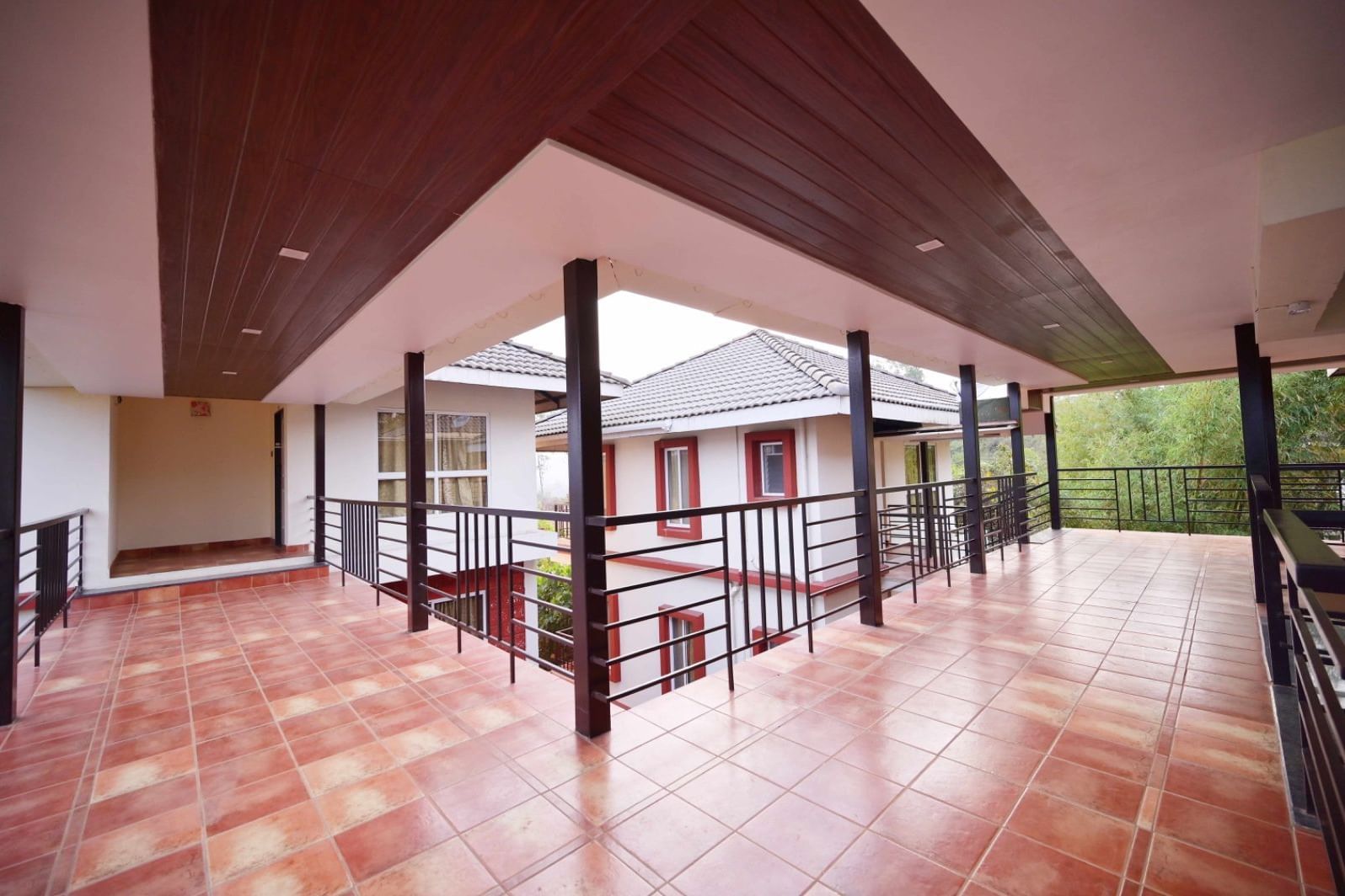 A partially covered outdoor walkway with tiled flooring, black railings in front of the luxury villas near Koyna Sanctuary at Forest Escapes