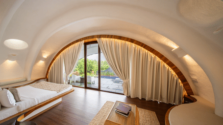 A bedroom features an arched ceiling with a king size bed, curtains over sliding glass doors, and a wooden coffee table on a rug at Amanzi Resort.