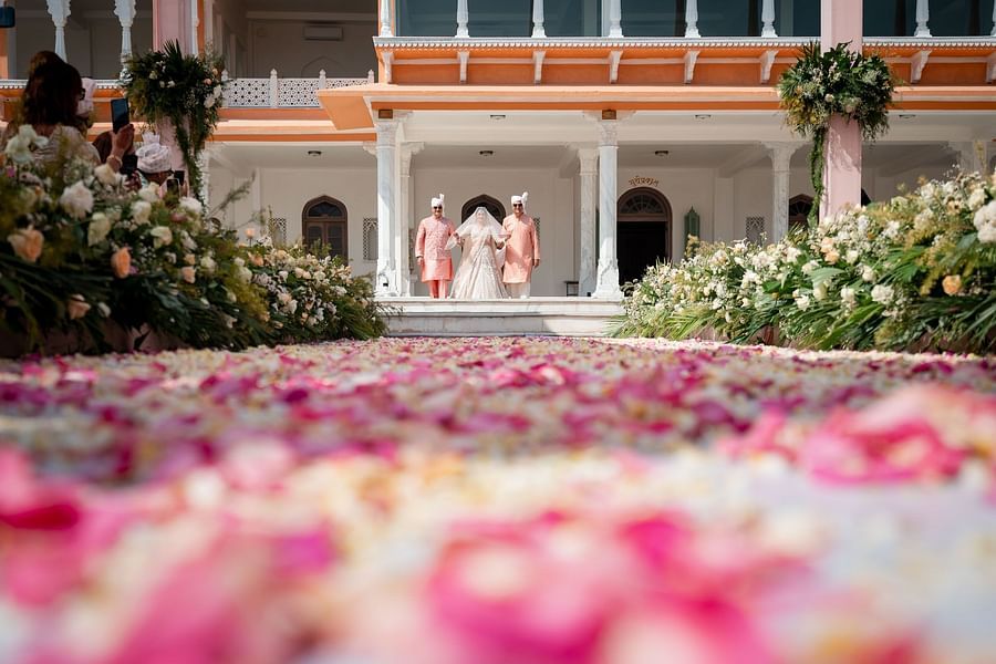 Bride walking down a petal-strewn aisle towards a grand palace entranceat  Fateh Vilas Collection Udaipur