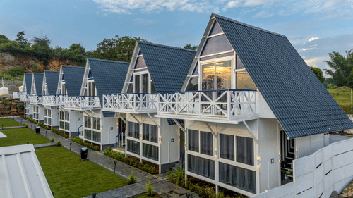 White A-frame cottages at a modern hillside resort with green lawns.