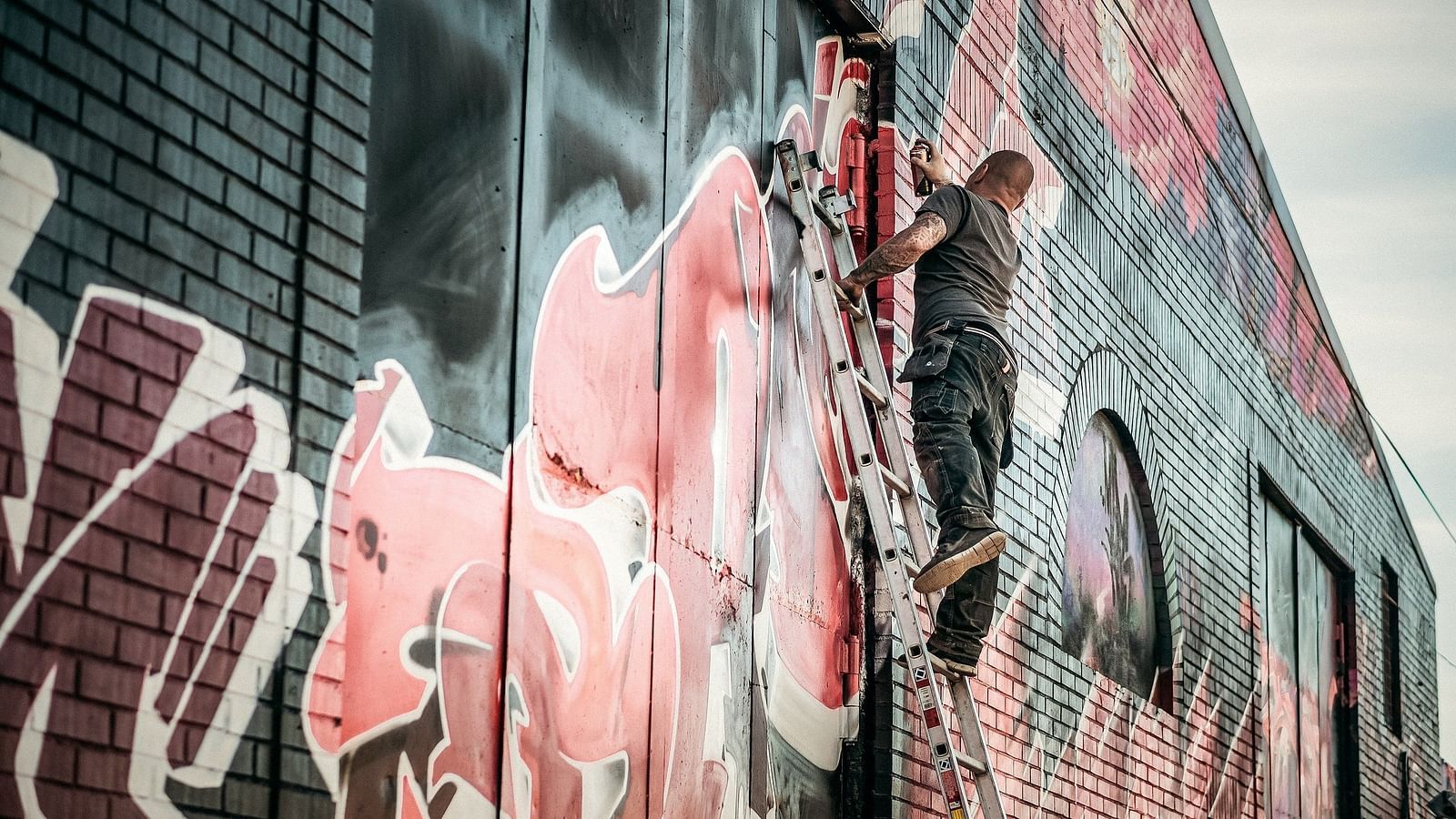 An overview of a graffiti artist on a ladder making a mural on a wall.
