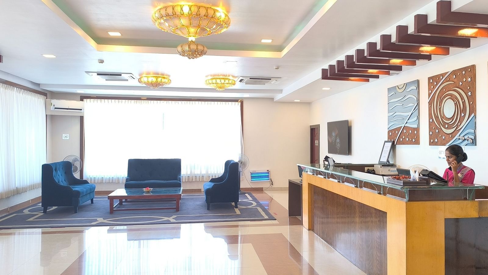 A well-illuminated hotel lobby featuring blue sofas for guest seating and a reception desk - Regency Tuticorin by GRT Hotels