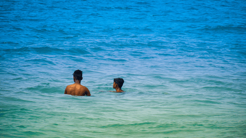 A zoomed in view of two people bathing in the Arabian Sea next to Colva Beach, one of the top 10 beaches in South Goa, in blue-green coloured waterbody.