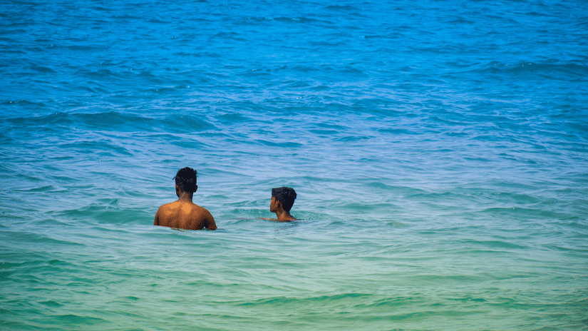 A zoomed in view of two people bathing in the Arabian Sea next to Colva Beach, one of the top 10 beaches in South Goa, in blue-green coloured waterbody.