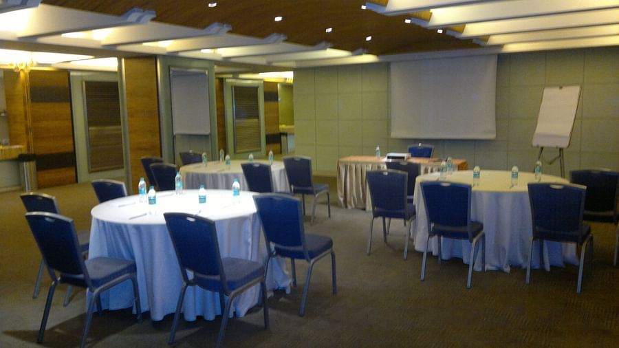 Image of an event space at Mirage Hotel featuring round tables and blue chairs along with a white board | Mirage Hotel