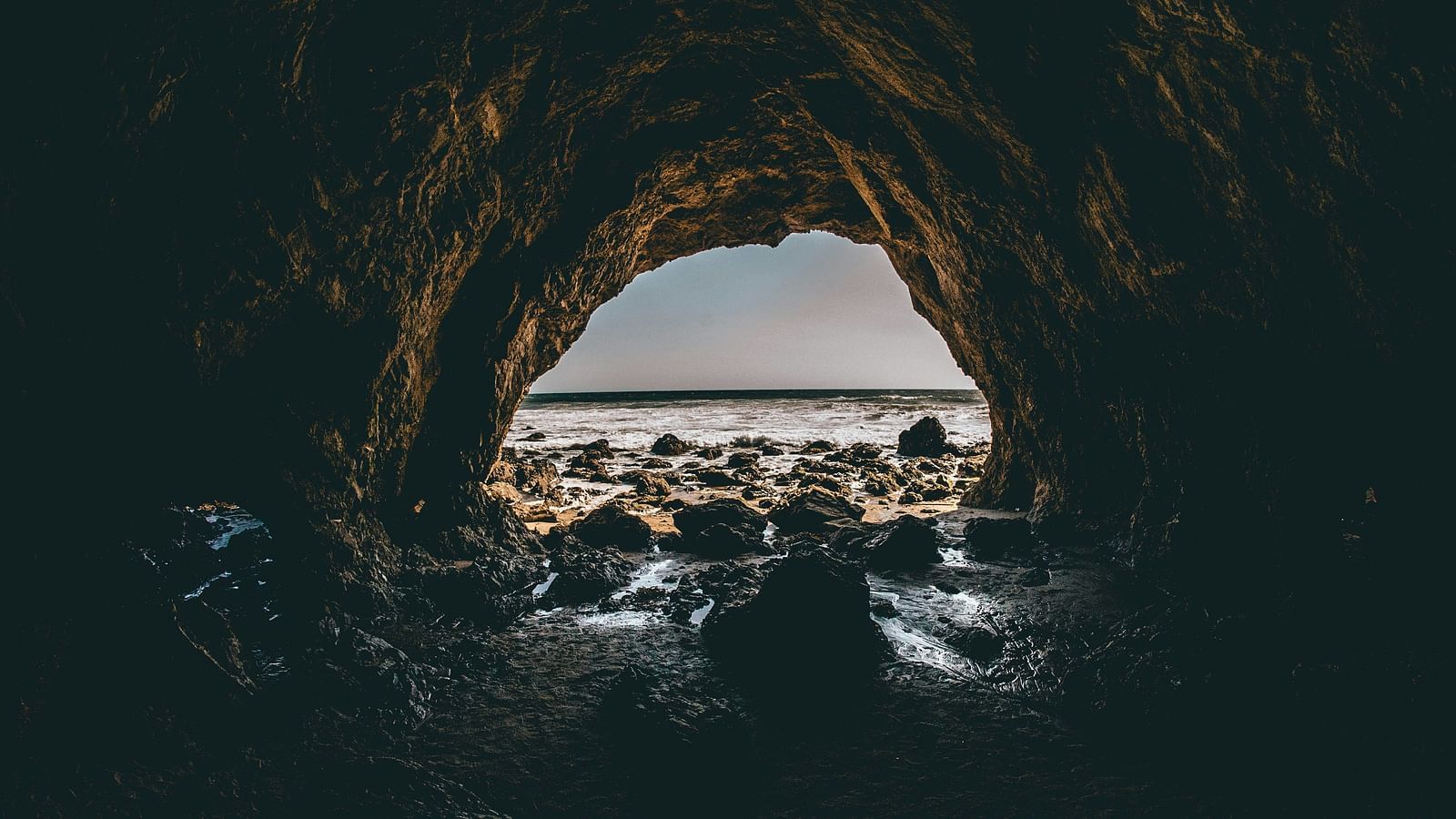 A view from inside a dark cave looking out towards a rocky beach and the ocean.
