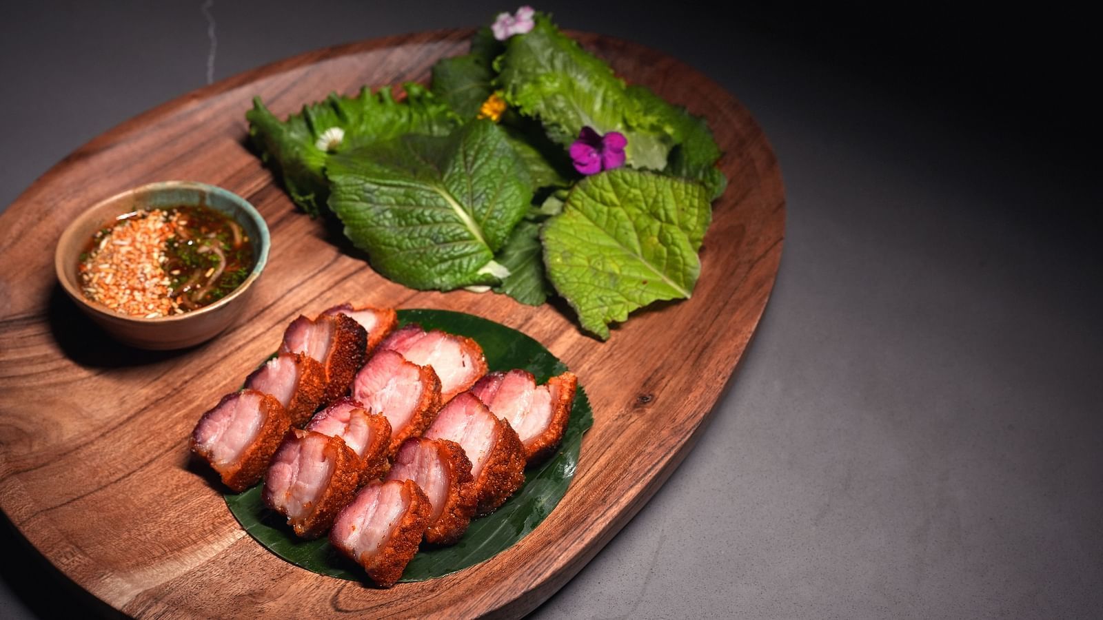 Crispy pork in a wooden serving dish with sides and veggies at Village 36