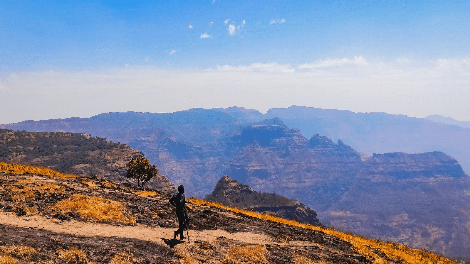 A man standing with a walking stick as he looks on to the valleys in the distance