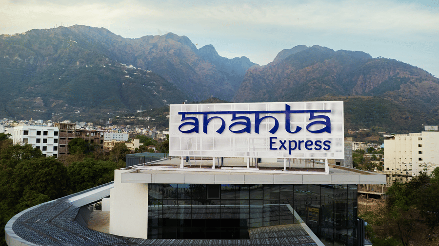 An exterior view of the hotel building with a large Ananta Express sign against a backdrop of mountains at Ananta Express, Katra.