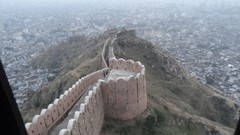 A long, winding stone wall snakes across a misty hilltop, overlooking the dense urban sprawl of the city below.
