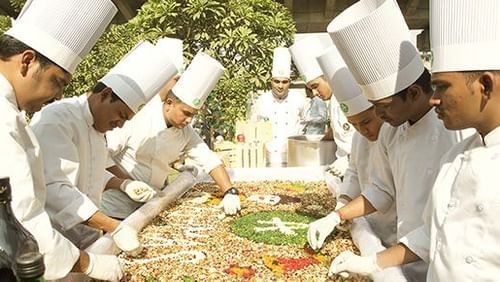 Our expert chefs gather around a table to carve our logo in food grains 