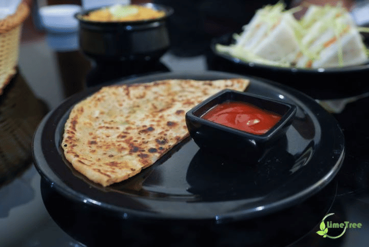 Paratha with tomato ketchup and vegetable sandwiches served on black plates