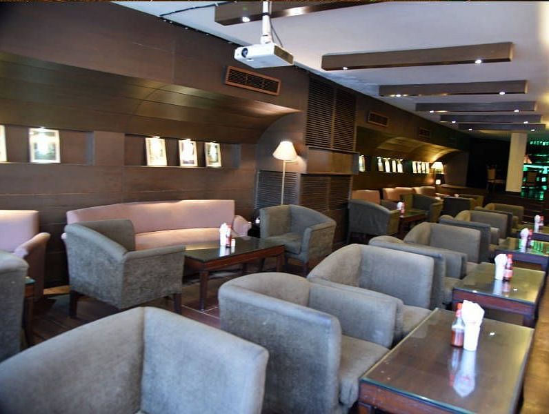 Several grey coloured cushioned arm chairs placed in front of individual tables with a projector hanging from the ceiling at 24 Karats Bar - Hotel Gold, Panipat