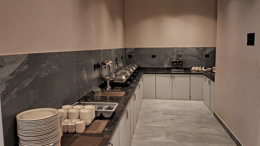 A buffet counter with stacked plates, cups, and food serving dishes set along a long countertop at Savyasaachii Hotel.