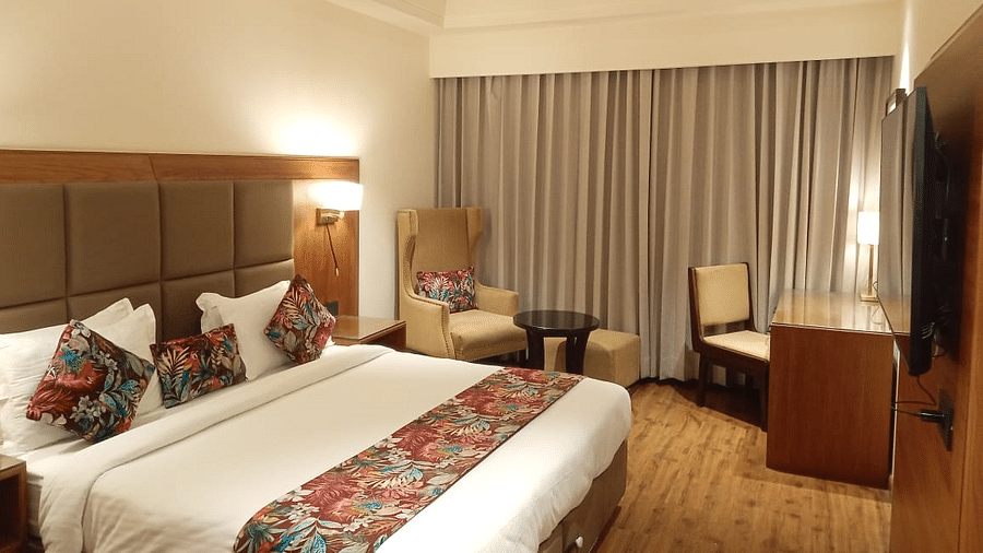 Modern hotel room with a king size bed, floral accents, a seating area with an armchair and table, a work desk, and a wall-mounted TV - Clarks Inn Express, Ludhiana