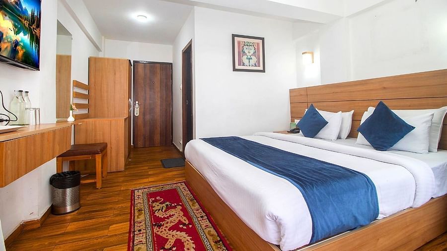 A room with double bed, Framed art work on the wall, TV, Wardrobe, Dustbin, Table and desk with two water bottles on the top at  Central Heritage Resort and Spa (Formerly Fortune ITC Resort) The Mall Road.