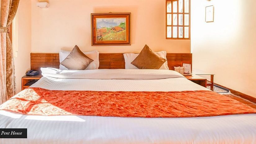 A Suite room featuring a spacious bed adorned with a wooden headboard and a painting positioned above it, at Sumitel Oriental, Gangtok.