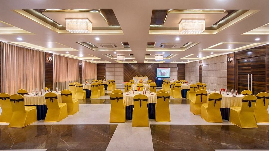 A spacious event hall at Lords Inn Porbandar, is prepared with round tables and chairs with yellow sashes, ready for guests.