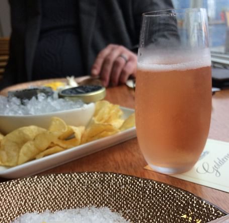 A close-up of a luxurious caviar serving with chips and a glass of rosé at a fine dining restaurant.