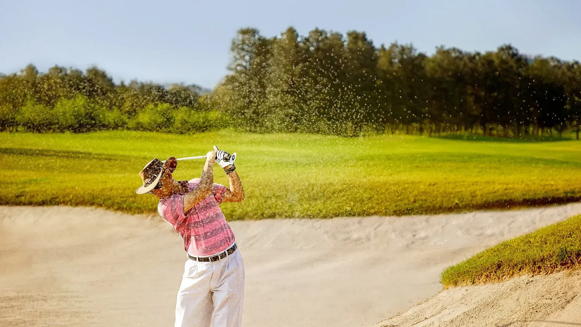 Golfer swinging a club in a sand bunker on a golf course surrounded by trees at Karma Chalets.