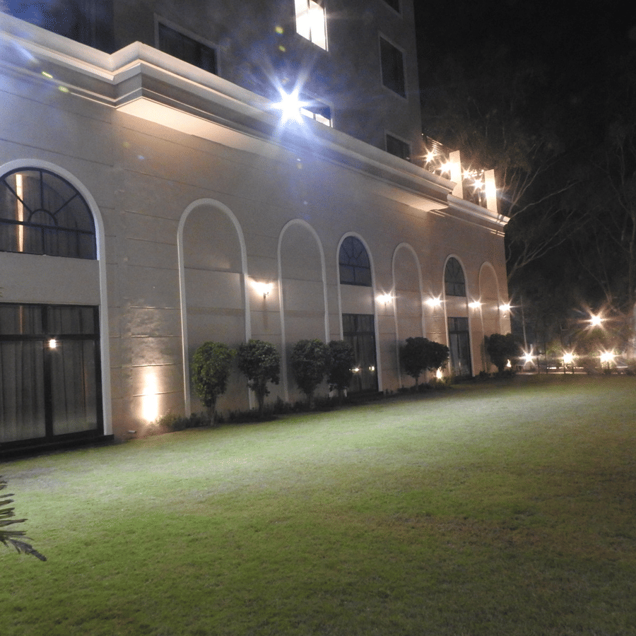Exterior of the at night, featuring a large, well-lit building with arched windows and a lush green lawn in the foreground lawn at Polo Hotel Agartala