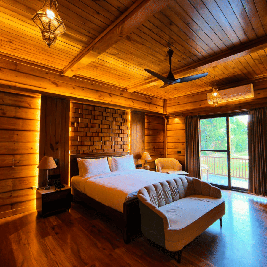 A bedroom at The Baagh Ananta Elite, Ranthambore featuring a king size bed, upholstered bench, single armchair, and glass door leading to a balcony.