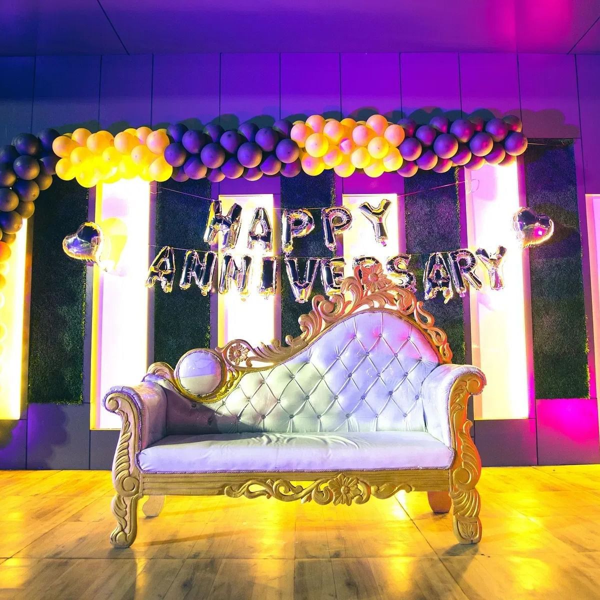 A wedding chair on the stage of a banquet hall with a decorated wall at the back at Daksh Resort & Amusement Park.