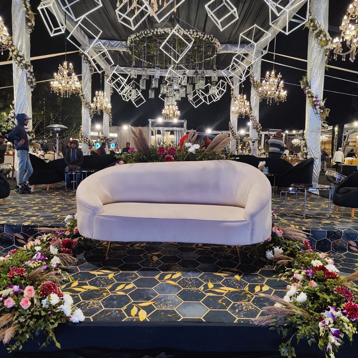A wedding stage with a white sofa, floral arrangements, and chandeliers.