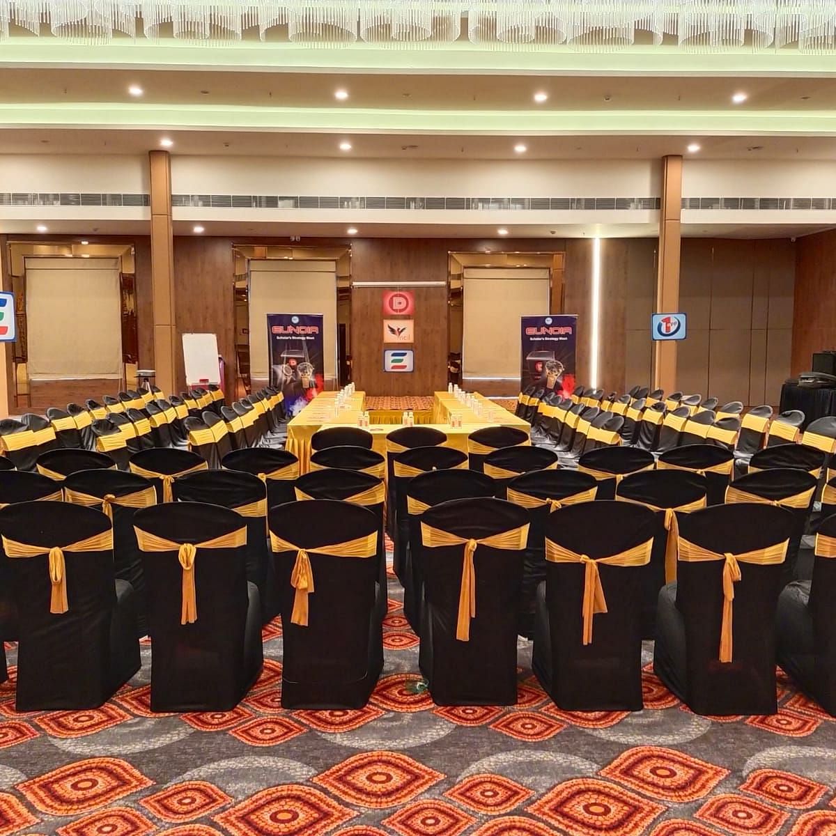 A well-lit and spacious event hall in Lords Eco Inn Shapar Rajkot, featuring neatly arranged chairs and carpeted floor.