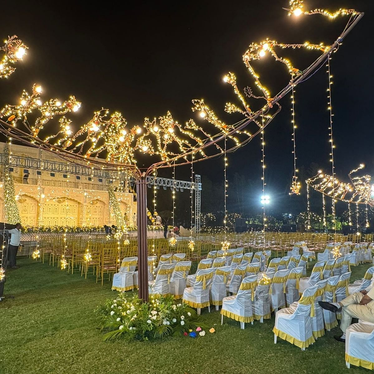 a beautifully decorated outdoor venue at night, featuring theatre style seating arrangements, a grand stage backdrop, and twinkling string lights everywhere at Lords Hrim Akshara Resort Basar