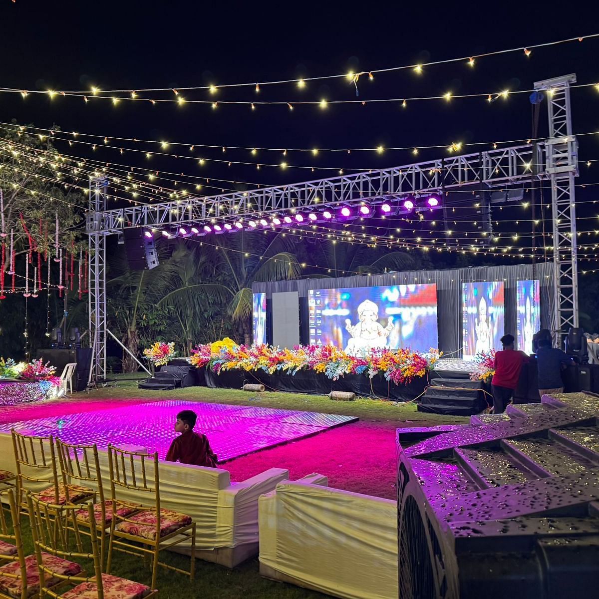 an outdoor event space with two stages, a well-lit decoration, and chairs arranged in a row with a complete audio visual system at Lords Hrim Akshara Resort Basar
