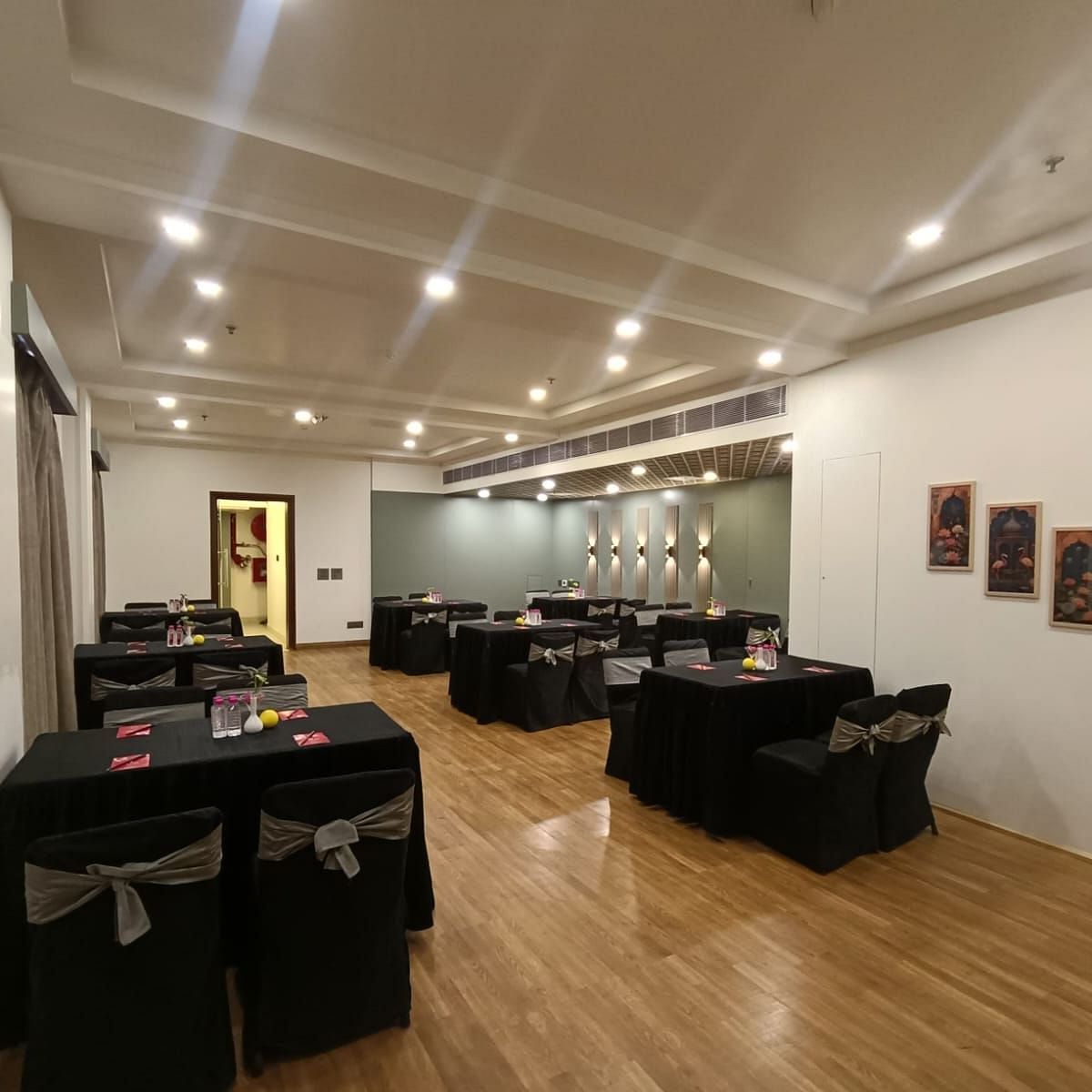 Conference room with rectangular tables covered with black satin covers and chairs under white ceiling lights at Lords Plaza Jaipur.