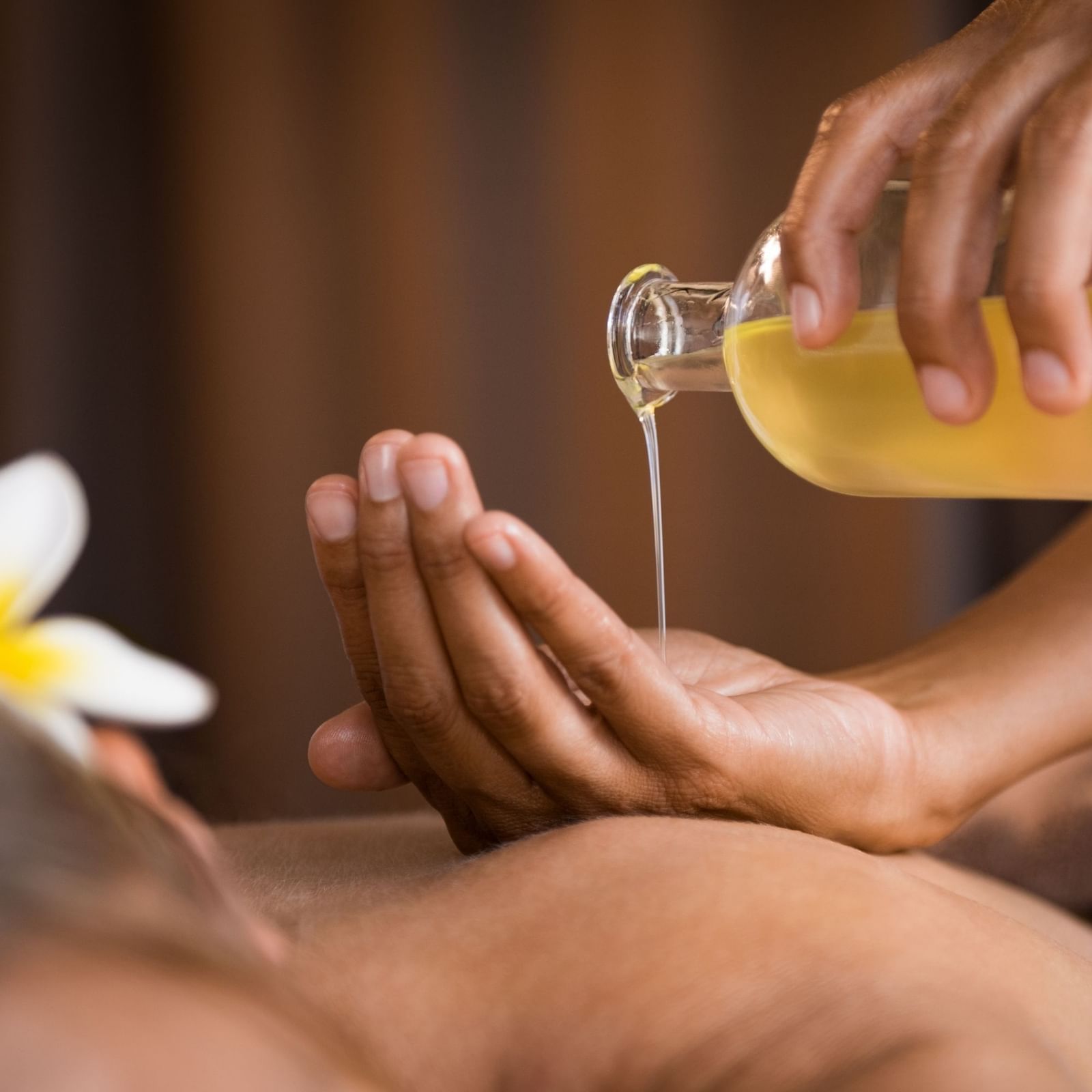 A person pouring oil on their hands to massage the back of the guest lying on their stomach at Rhythm Lonavala