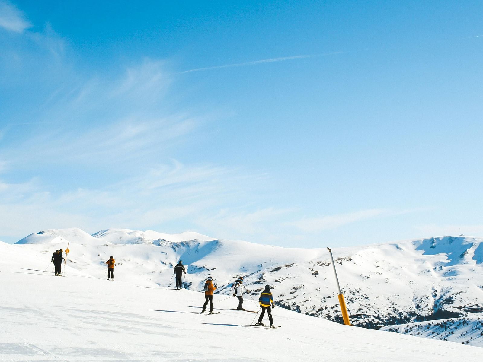 people scattered around warmly dressed with their skiing gears on a snowy plain with mountains in the background